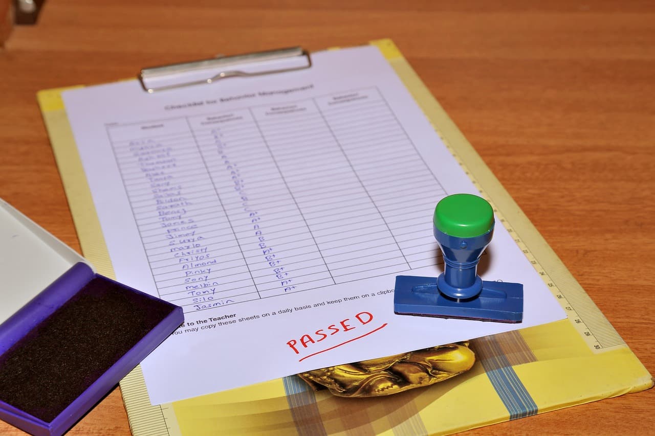 Clipboard with a class list of A and B letter grades, a PASSED note in red and a rubber stamp