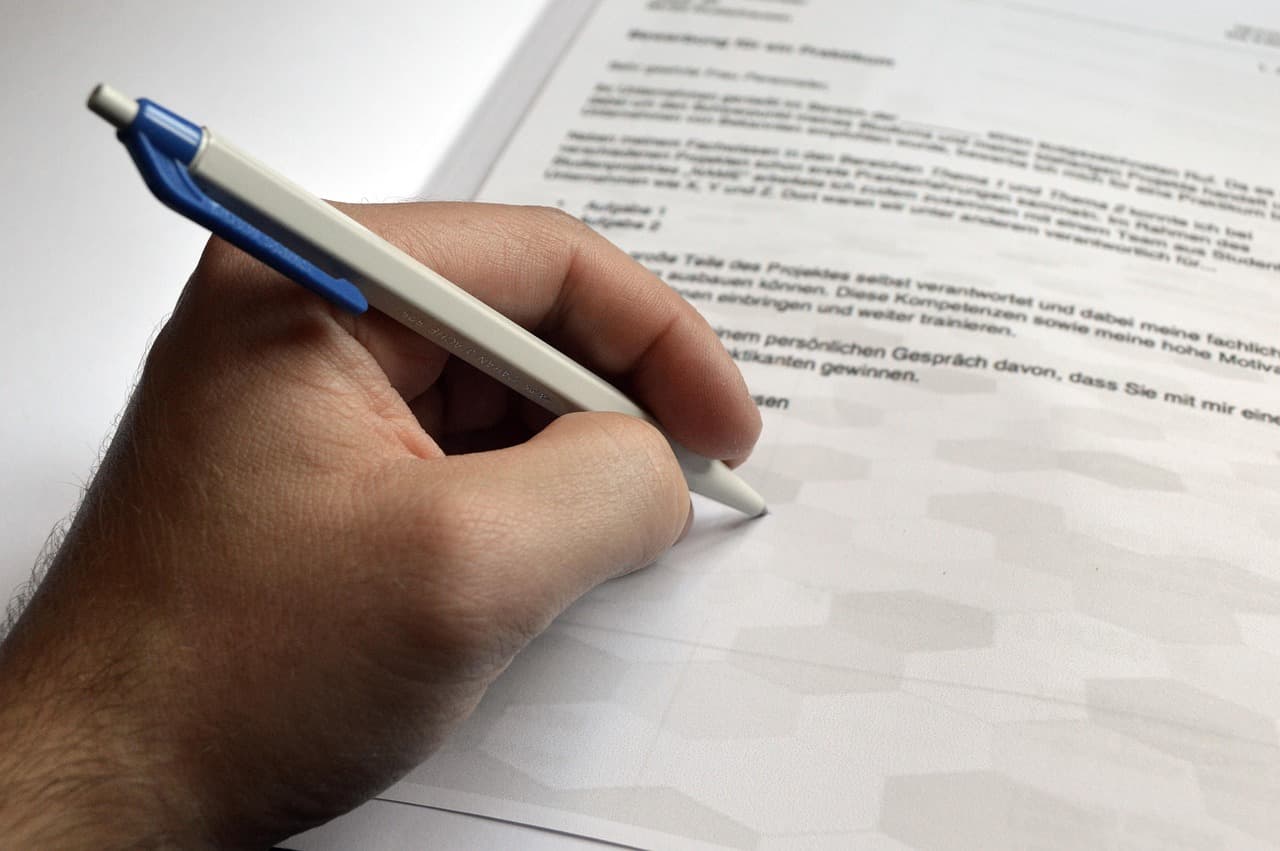 A hand holding a pen over a printed job application letter on a desk