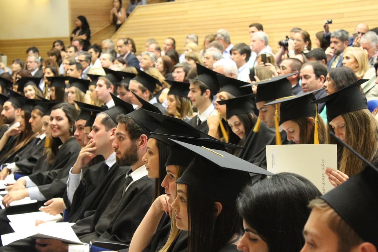 Graduates in caps and gowns holding rolled diplomas tied with ribbon