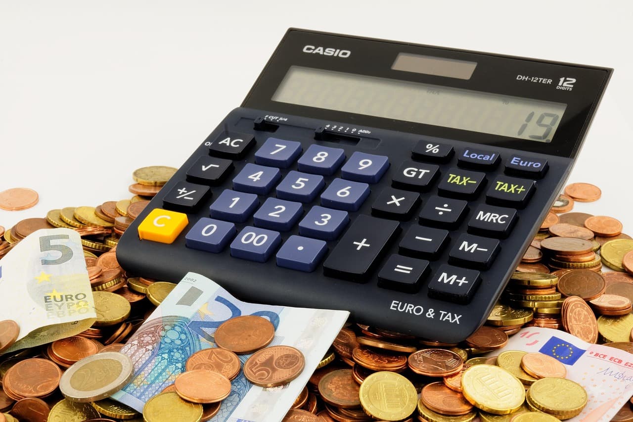 Euro coins and banknotes next to a piggy bank and a calculator on a desk